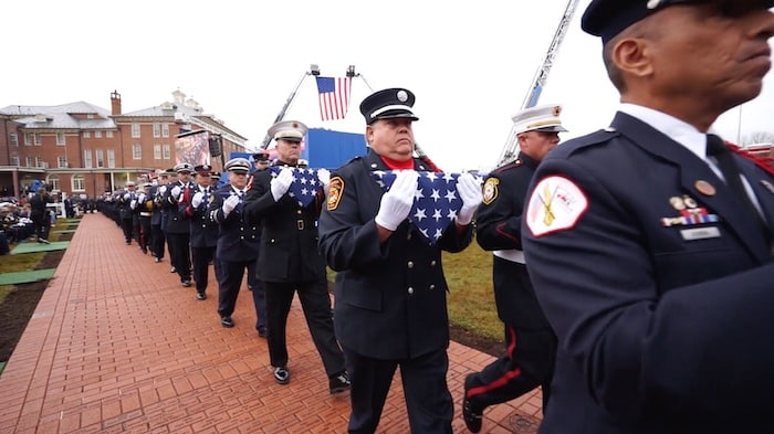2023 national fallen firefighter foundation march holding folded US flags under raised US flag between truck ladders