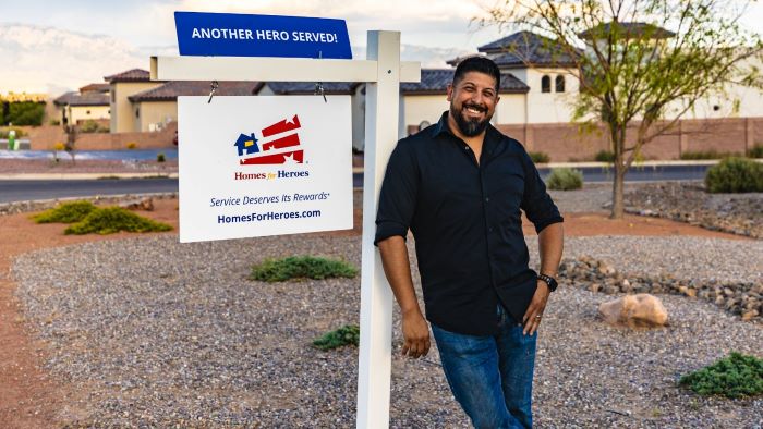 Homes for Heroes real estate specialist Mario Montoya leans on for sale sign in neighborhood