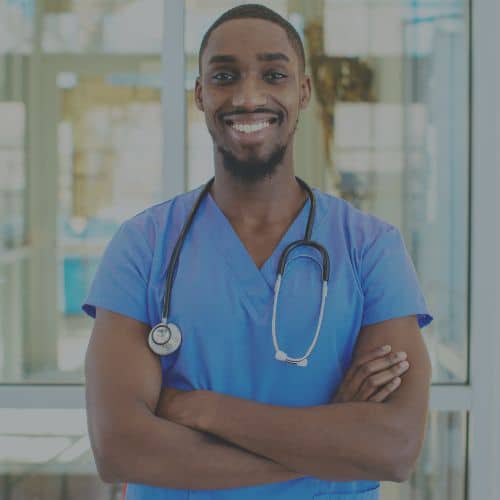 man certified nursing assistant smiling arms folded blue scrubs in hallway