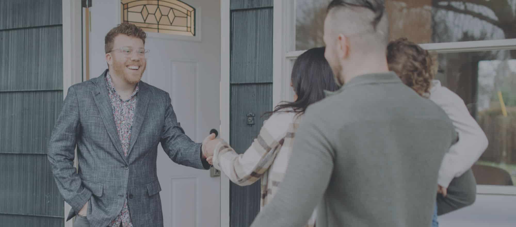 real estate agent greets client couple with child at front door of potential home for sale to do walk through