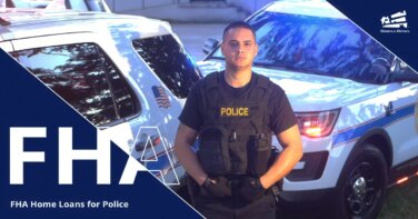 male police officer wearing bullet proof vest that says police standing in front of two police cars with blue lights flashing