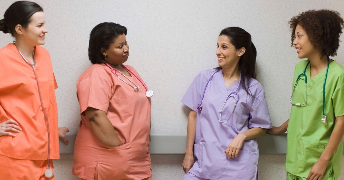 Four nurses wearing different color scrubs talking