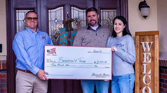 Veteran couple holding big check in front of their new home