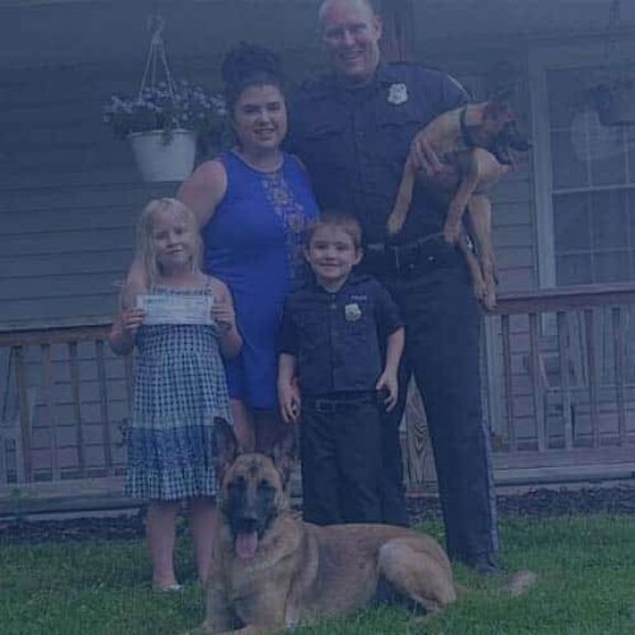 law enforcement family mother father two children two dogs standing in front of home holding Homes for Heroes Hero Rewards Savings check