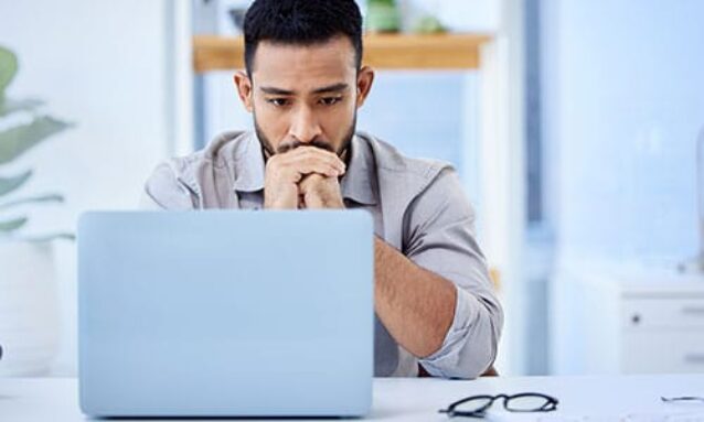 Male real estate agent sitting at a desk in front of a laptop thinking of ways to make lead gen easier