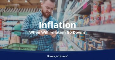 man holding cellphone in grocery store checking prices with basket on arm wondering when will inflation go down Homes for Heroes