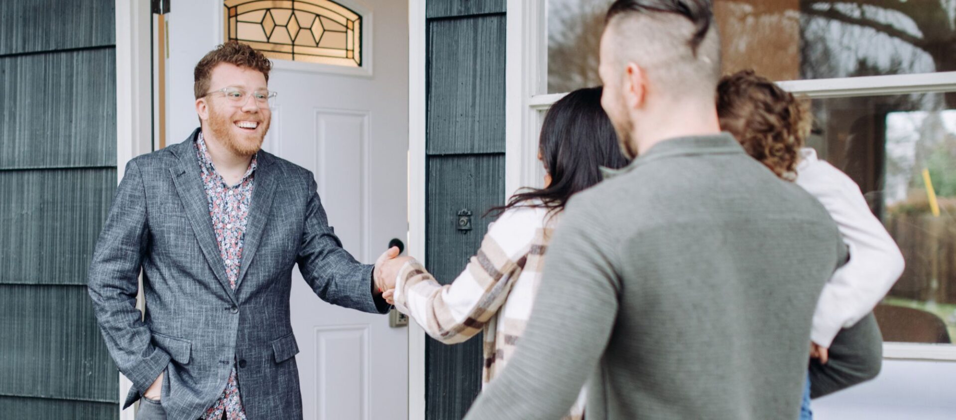 real estate agent greets client couple with child at front door of potential home for sale to do walk through