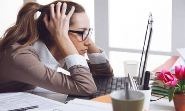 real estate agent sitting at desk hands on head staring at laptop overwhelmed by too much work needs to get real estate marketing emails set up