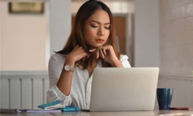 woman agent sitting at table working on laptop thinking about her real estate social media marketing priorities