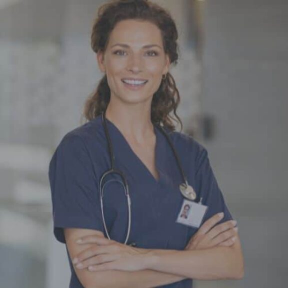 woman registered nurse folded arms smiling long hair navy scrubs name tag in hospital hallway