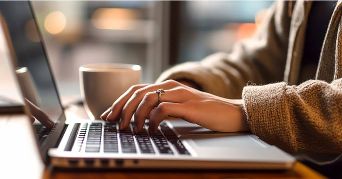 blogger sitting at table at coffee shop typing on laptop writing blog post draft