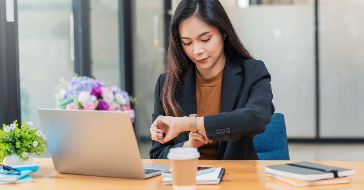 female real estate agent sitting at desk open laptop checking watch for websites appointment Homes for Heroes