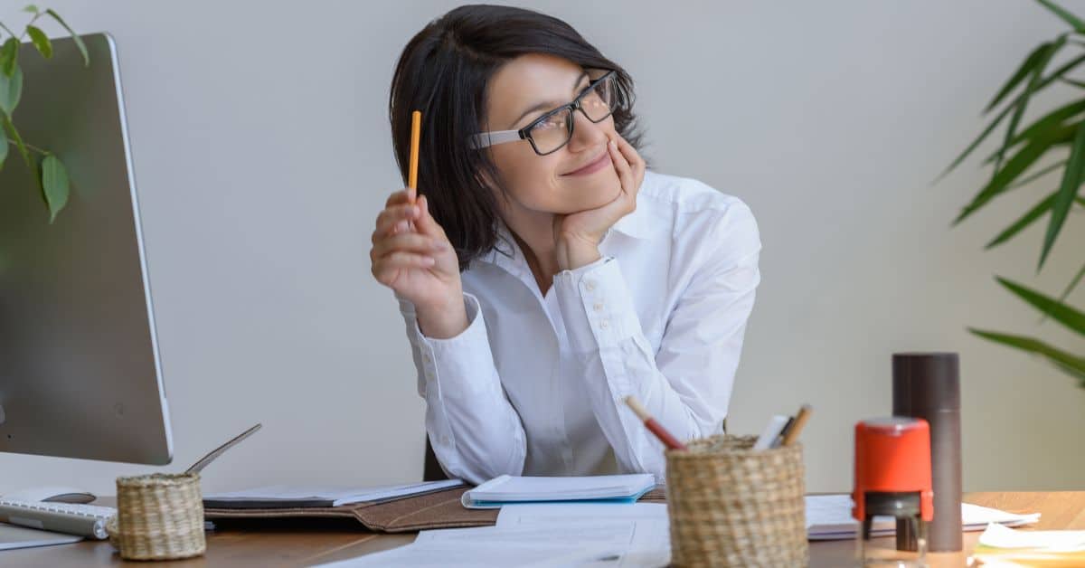 female real estate agent sitting at desk in office smirking thinking about building website Homes for Heroes