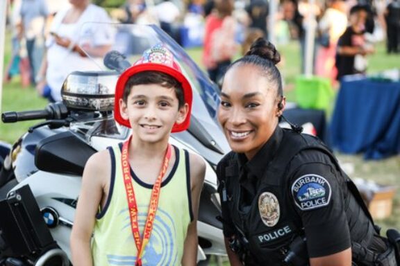 young man wearing fire hat with Burbank officer standing next to motorcycle